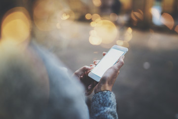 Woman holding hands smartphone in night atmospheric city.Female hands using mobile phone.Closeup on blurred background.Flares, bokeh effects.