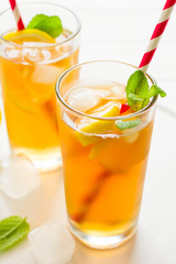 Glasses of iced tea with lemon slices and mint on white wooden background