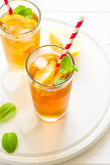 Glasses of iced tea with lemon slices and mint on white wooden background