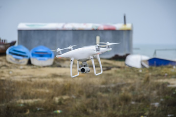 Drone flying in front of a blurry background of boats and depot.
