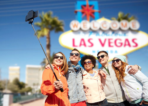 summer holidays, vacation, tourism and travel concept - group of smiling teenage friends taking picture by smartphone selfie stick over welcome to fabulous las vegas sign background