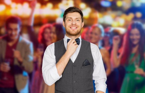 party, people and style concept - happy man in festive suit dressing for party and adjusting bowtie over night club background