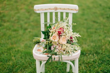 beautiful wedding  bouquet lying on old white chair standing on the grass.