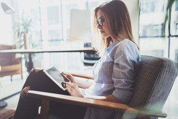 Handsome young blonde wearing glasses and using electronic touch tablet computer on sunny workplace.Horizontal. Blurred background.