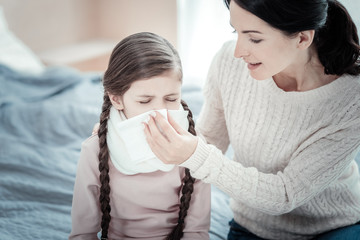 Trust me. Caring lovely attentive mother sitting in the bright bedroom holding a napkin and taking care of her daughter.