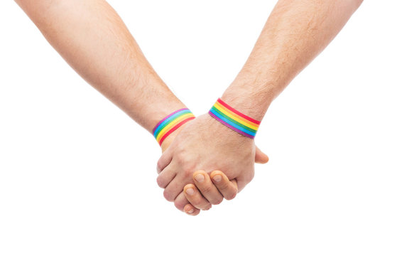 lgbt, same-sex relationships and homosexual concept - close up of male couple wearing gay pride rainbow awareness wristbands holding hands