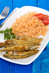fried smelts with tomato rice on white dish on blue background