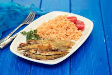 fried smelts with tomato rice on white dish on blue background
