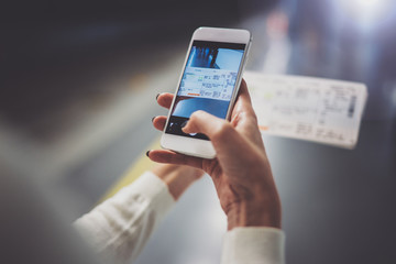 Closeup view of woman on transit platform using smartphone for make photo of train ticket while waiting rail train on metro station.