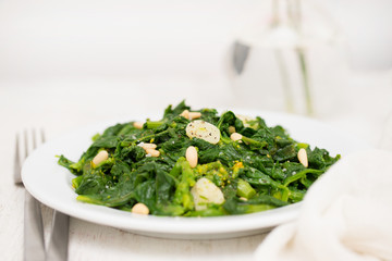 greens with garlic on white plate on wooden background