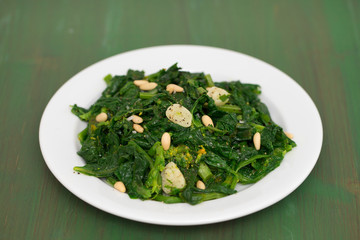 greens with garlic on white plate on wooden background