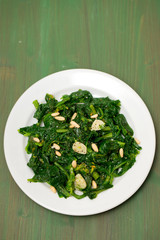 greens with garlic on white plate on wooden background © Natalia Mylova
