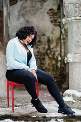 Stylish african american plus size model sitting on red chair outdoor.