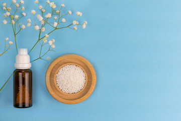 Homeopathic grains in a glass bottle, and on a wooden plate, and a green grass branch.