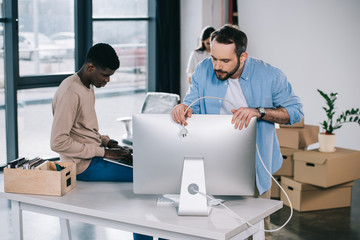 man holding plug from desktop computer while relocating with colleagues at new workplace