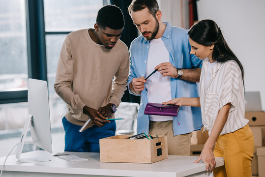 multiethnic coworkers unpacking box with office supplies at new workplace - Powered by Adobe