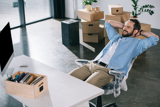 happy businessman sitting with hands behind head and looking away in new office during relocation