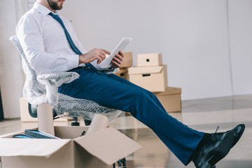 cropped shot of businessman using digital tablet while sitting in new office during relocation