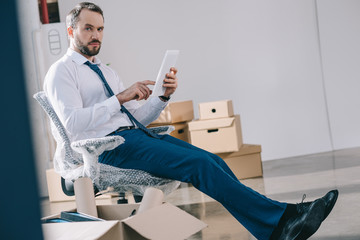 bearded businessman using digital tablet and looking at camera while sitting in new office