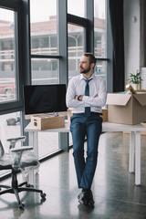 businessman with crossed arms sitting on table and looking away in new office