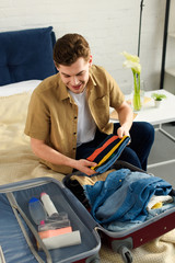 handsome smiling man packing clothes for vacation