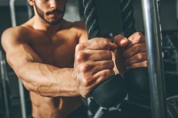 Muscular man working out in gym doing exercises with triceps rope