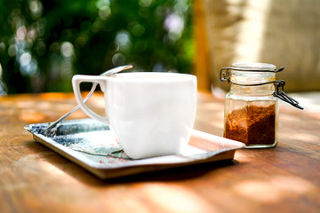 A cup of coffee on a wooden table. A fragrant drink with a teaspoon of foam and brown sugar. A metal tray in the form of a stand. Blurred background, top and side view with copy space.
