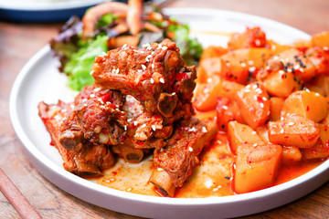 Fried pork ribs with potatoes and salad. On a white plate with a knife and fork. Wooden background - a table. Close up view with copy space