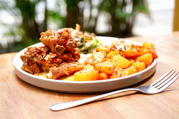 Fried pork ribs with potatoes and salad. On a white plate with a knife and fork. Wooden background - a table. Close up view with copy space