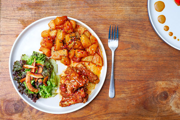 Fried pork ribs with potatoes and salad. On a white plate with a knife and fork. Wooden background - a table. Top view with copy space
