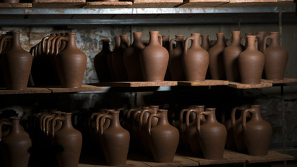 Fototapeta na wymiar pottery, workshop, ceramics art concept - closeup on young ceramist hands with unbaked clay jug, craftsman stand at a workplace, hands holds the clay cup and tools
