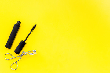 Basic products for eyelashes makeup. Mascara and eyelash curler on yellow background top view copy space