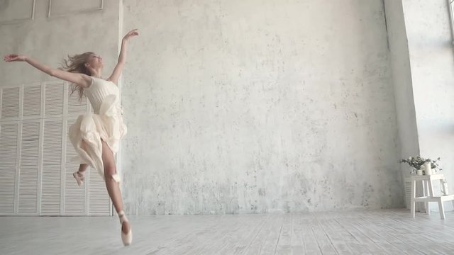 beautiful young ballerina dancing in a light, flying dress on the background of a large window. the ballet dancer is spinning on tiptoes and jumping high. slow motion