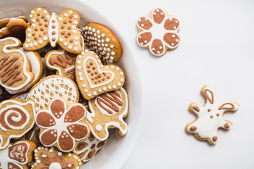 Gingerbread cookies in the shape of Easter bunny, heart, butterfly and flowers, covered with white and chocolate icing-sugar, in a white dish on a white surface