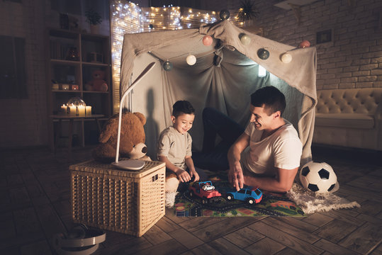 Father And Son Are Playing With Toy Cars On Carpet Road At Night At Home.