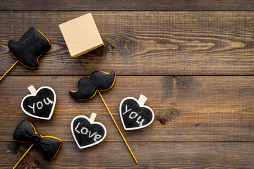 Gift for man on birthday. Gift box among cookies in shape of moustache, hat, bow tie and hearts with lettering love you on dark wooden background top view copy space