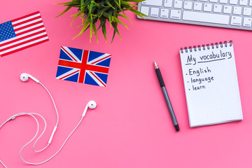 Learn new english vocabulary. Learn landuage concept. Computer keyboard, british and american flags, notebook for writing new vocabulary on pink background top view