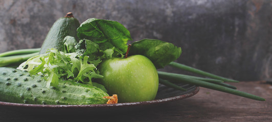 green fresh vegetables: cucumber, lettuce, onion, avocado, apple on old background
