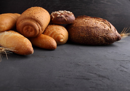 white, gray and rye bread, baguette, roll with sesame seeds on a black background