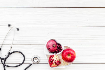 Naklejka na ściany i meble Products good for heart and blood vessels. Vegetables, fruits, nuts in heart shaped bowl near stethoscope on white wooden background top view copy space