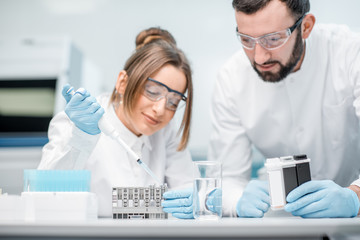 Laboratory assistants in uniform and protective glasses working with test tubes in the medical laboratory