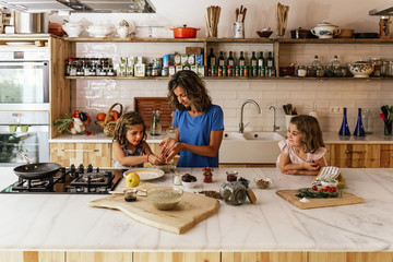 Little sisters cooking with her mother in the kitchen.