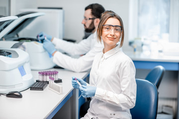 Portrait of a young female laboratory assistant making analysis with test tubes and analyzer...