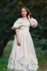 Beautiful brunette in a vintage dress. A nice young girl in a classic outfit. A woman in a stylish vintage dress. Style of the queen. Classical attire of the princess. A woman is walking in the woods.