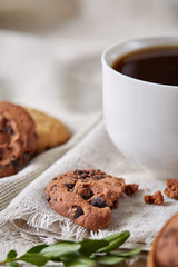 Morning coffee in white cup, chocolate chips cookies on homespun napkin, close-up, selective focus
