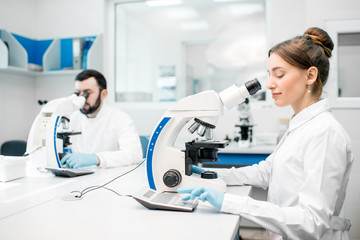 Two medics in uniform working with microscope making analysis at the laboratory office