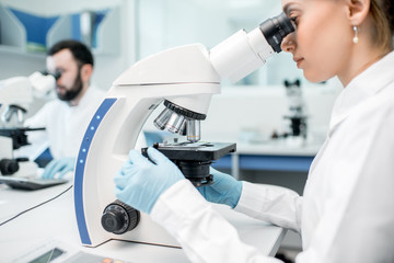 Two medics in uniform working with microscope making analysis at the laboratory office