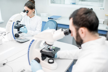 Two medics in uniform working with microscope making analysis at the laboratory office