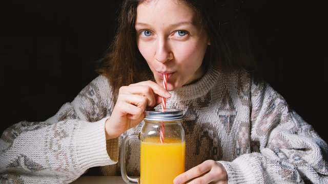 Young beautiful girl drinking fresh orange juice in a glass bottle with a straw