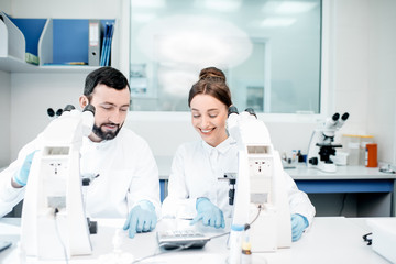 Couple of medics in uniform working with microscope making analysis at the laboratory office